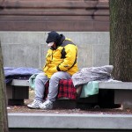 Homeless man sitting on bench with sleeping back
